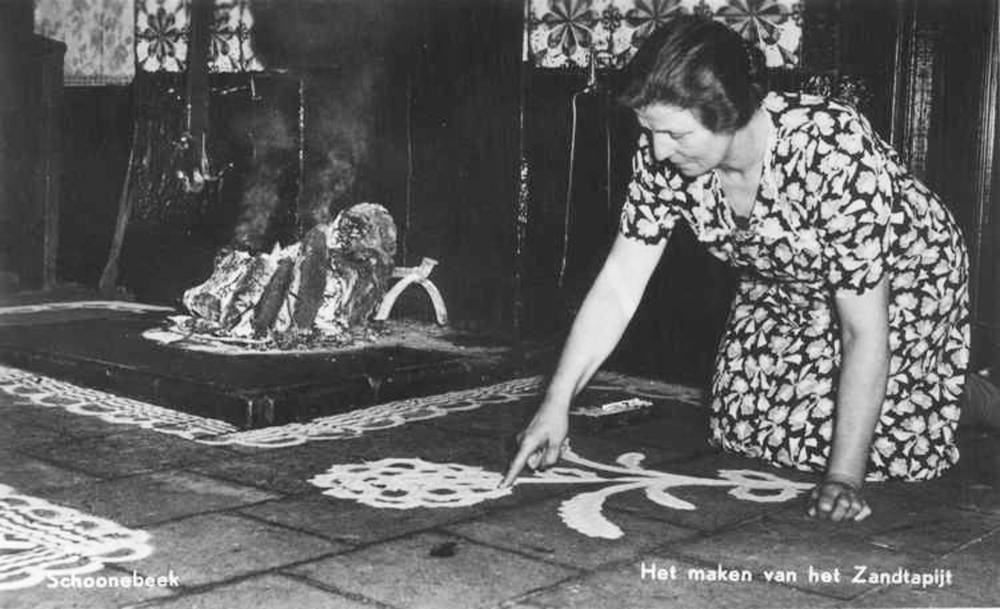 Woman drawing a sand carpet, Schoonebeek, NL. Drenthe Archive, collection Mulder. One example is the 'Zandtapijt' which has it's origins in NL and parts of BE, for special events. Sand was used as a tool to paint patterns on the ground - which were wiped away the same evening.